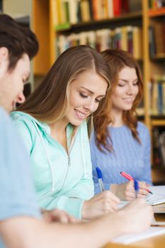 people, knowledge, education and school concept - group of happy students preparing to exam and writing in library