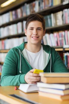 people, education, technology and school concept - male student with smartphone and books in library