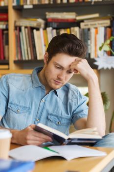 people, knowledge, education and school concept - male student reading book in library