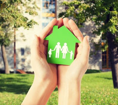 real estate and family home concept - closeup picture of female hands holding green paper house with family