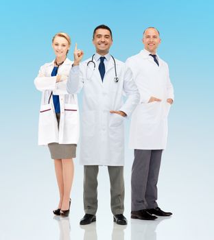 healthcare, announcement, people and medicine concept - group of smiling doctors in white coats pointing finger up and warning over blue background
