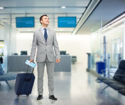 business trip, traveling, luggage and people concept - happy businessman in suit with travel bag and air ticket over airport background