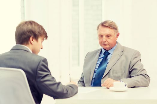 business, technology and office concept - older man and young man signing papers in office