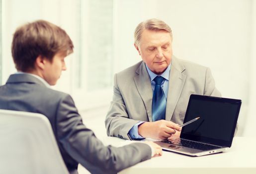 business, advertisement, technology and office concept - older man and young man with laptop computer in office