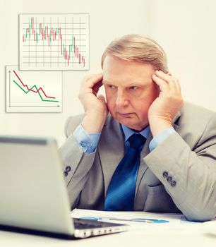 business, technology and office concept - upset older businessman with laptop and charts in office