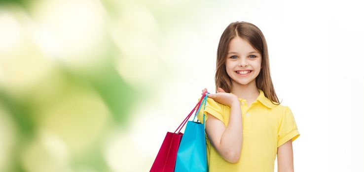 shopping, happiness and people concept - smiling little girl in yellow dress with shopping bags