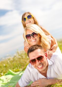 summer holidays, family, child and happy people concept - smiling family in sunglasses lying on blanket outdoors