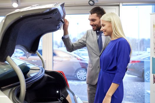 auto business, car sale, technology and people concept - happy couple with car dealer in auto show or salon