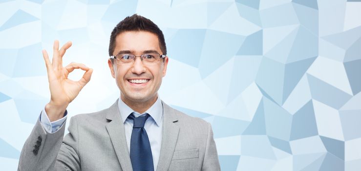 business, people, vision and office concept - happy smiling businessman in eyeglasses and suit showing ok gesture over gray graphic low poly background