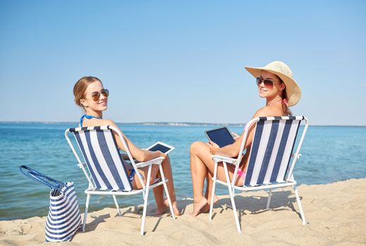 summer vacation, travel, technology and people concept - happy women with tablet pc computers sunbathing in lounges on beach