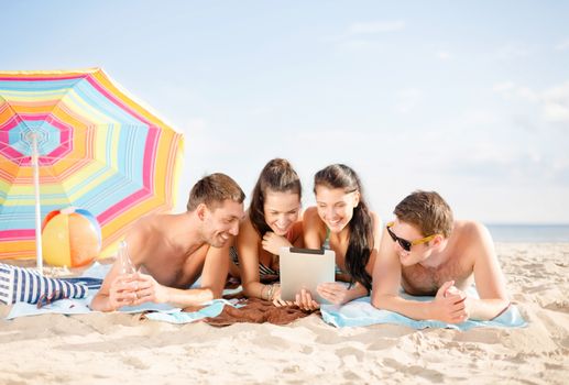 summer holidays, vacation, technology and people concept - group of happy friends with tablet pc computer sunbathing on beach