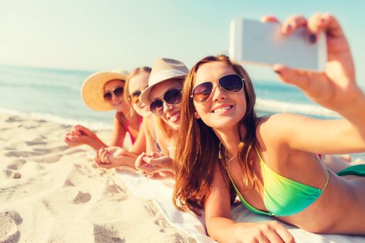 summer vacation, travel, technology and people concept - group of smiling women in sunglasses and hats making selfie with smartphone on beach