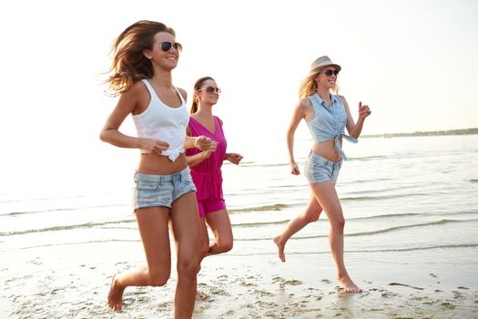 summer vacation, holidays, travel and people concept - group of smiling young women in sunglasses and casual clothes running on beach