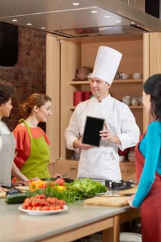 cooking class, culinary, food, technology and people concept - happy women with chef cook showing blank tablet pc screen in kitchen