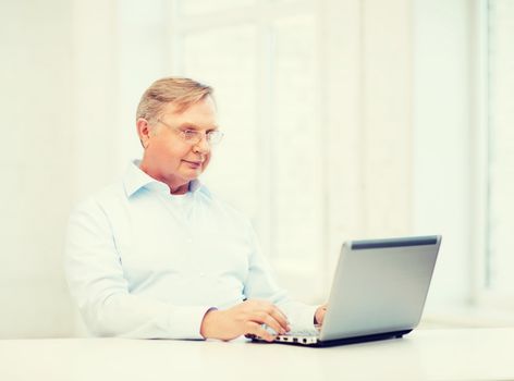 technology, oldness and lifestyle concept - old man in eyeglasses working with laptop computer at home