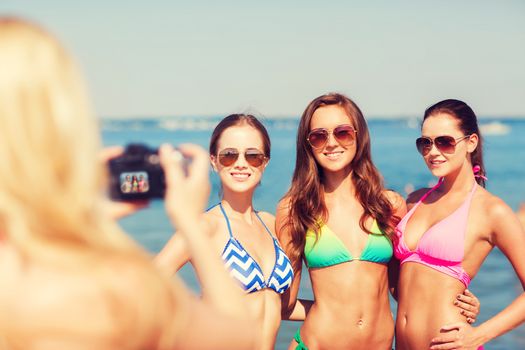 summer vacation, gesture, travel and people concept - group of smiling young women photographing by camera and waving hands on beach