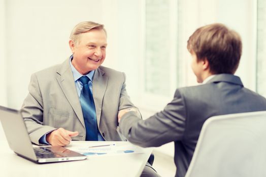 business, technology and office concept - older man and young man shaking hands in office
