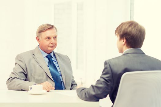 business, technology and office concept - older man and young man signing papers in office