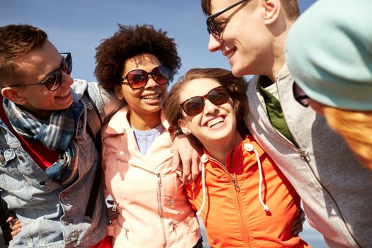 tourism, travel, people, leisure and teenage concept - group of happy friends in sunglasses hugging and laughing on city street