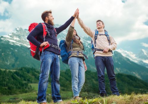 travel, tourism, hike, gesture and people concept - group of smiling friends with backpacks making high five over alpine mountains background