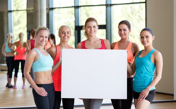 fitness, sport, training, gym and lifestyle concept - group of women witn white blank billboard in gym