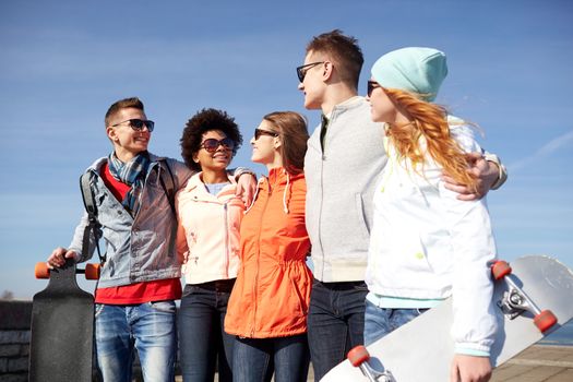 people, leisure and sport concept - group of happy teenage friends with longboards talking on city street