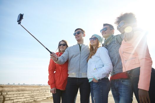 tourism, travel, people, leisure and technology concept - group of smiling teenage friends taking selfie with smartphone and monopod on city street