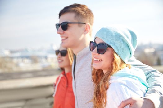 tourism, travel, people and leisure concept - group of happy teenage friends in sunglasses hugging on city street