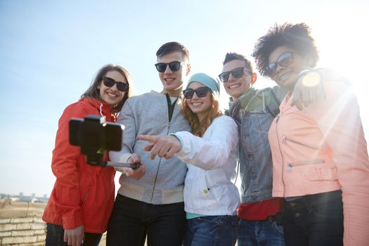 tourism, travel, people, leisure and technology concept - group of smiling teenage friends taking selfie with smartphone and monopod on city street