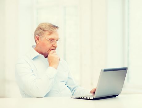 technology, oldness and lifestyle concept - old man in eyeglasses working with laptop computer at home