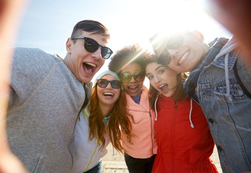 tourism, travel, people, leisure and technology concept - group of happy laughing teenage friends taking selfie outdoors