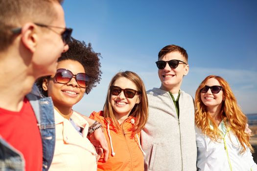 tourism, travel, people, leisure and teenage concept - group of happy friends in sunglasses hugging and talking on city street