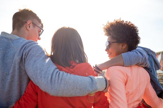 tourism, travel, people, leisure and teenage concept - group of happy friends hugging and talking on city street from back