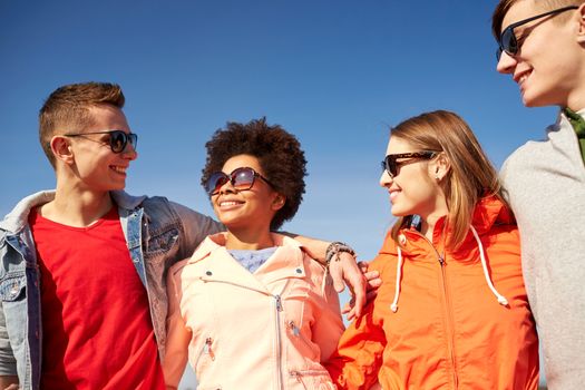 tourism, travel, people, leisure and teenage concept - group of happy friends in sunglasses hugging and talking on city street