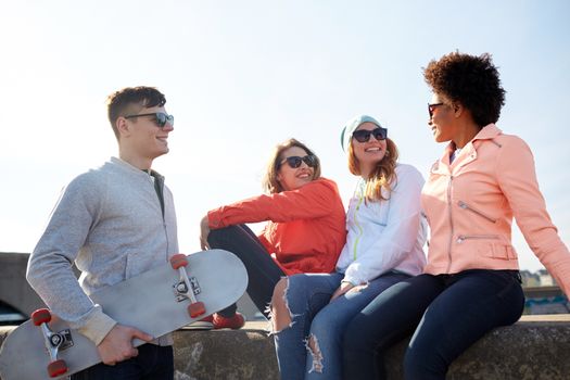 people, leisure and sport concept - group of happy teenage friends with longboard talking on city street