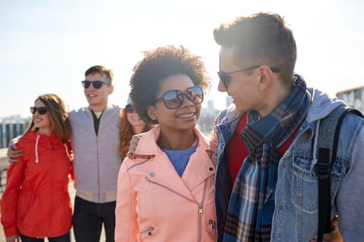 tourism, travel, people, leisure and teenage concept - group of happy friends in sunglasses hugging and talking on city street