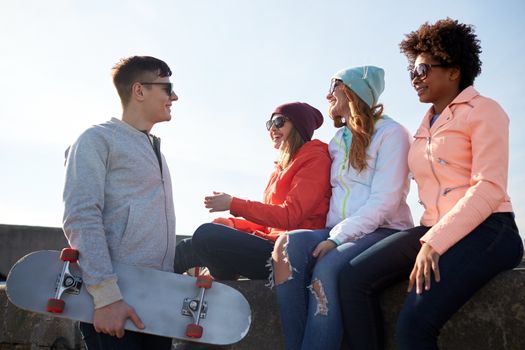 people, leisure and sport concept - group of happy teenage friends with longboard talking on city street