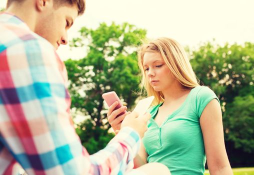 vacation, technology and friendship concept - couple with smartphones in park