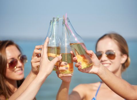 summer vacation, holidays, party, travel and people concept - close up of happy young women with drinks clinking bottles on beach