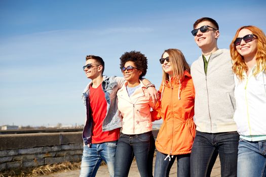 tourism, travel, people and leisure concept - group of happy teenage friends walking along city street