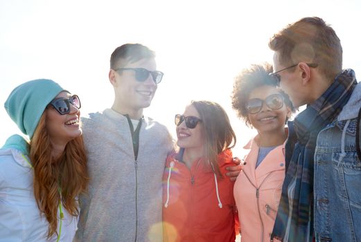 tourism, travel, people, leisure and teenage concept - group of happy friends in sunglasses hugging and talking on city street