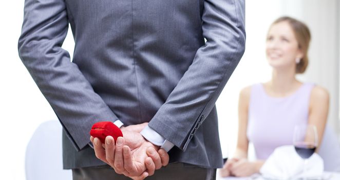 couple, love, proposal and holiday concept - close up of man hiding red box behind from woman at restaurant