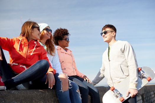 people, leisure and sport concept - group of happy teenage friends with longboard talking on city street