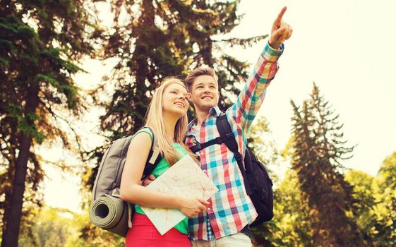 hiking, travel, vacation and friendship concept - smiling couple with map and backpack in nature