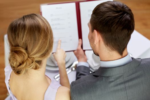 restaurant, food, eating and holiday concept - close up of happy couple with menu choosing dishes at restaurant