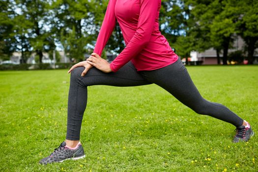 fitness, sport, training, people and lifestyle concept - close up of woman stretching leg and doing lunge in park