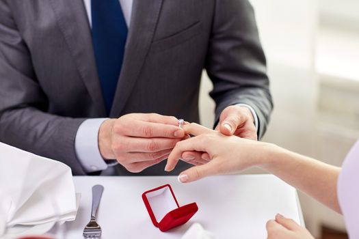 couple, love, engagement and holiday concept - close up of man putting ring to his fiance finger at restaurant