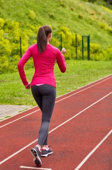 fitness, sport, training, people and lifestyle concept - african american woman running on track outdoors from back