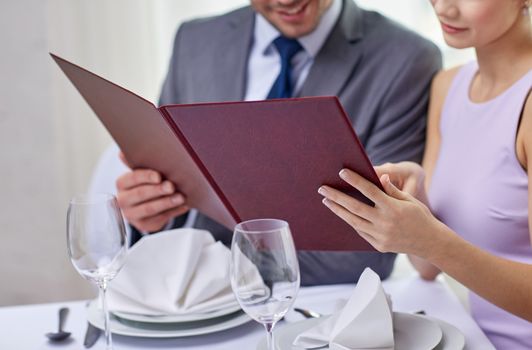 restaurant, food, eating and holiday concept - close up of happy couple with menu choosing dishes at restaurant