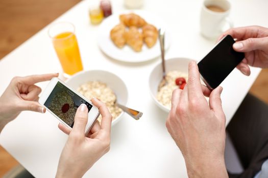 food, eating, people, technology and healthy food concept - close up of couple having breakfast and taking picture of food with smartphones at home